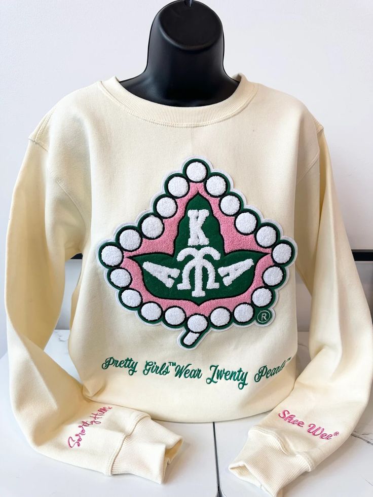 a white sweatshirt with green and pink designs on it's chest, sitting on a black mannequin head