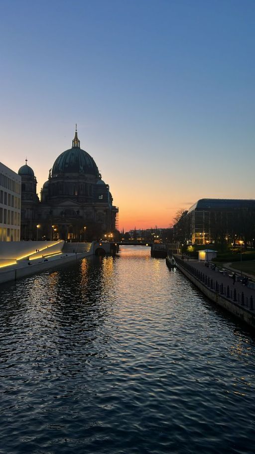 the sun is setting over some buildings on the side of a river with water in front of it