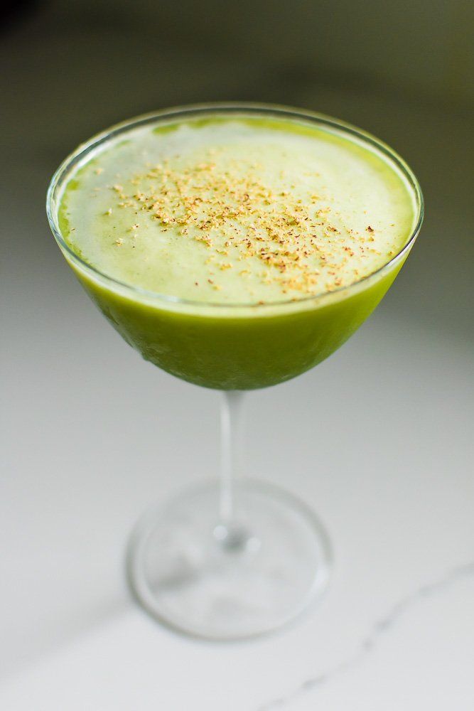 a green drink with sprinkles in a glass on a white counter top