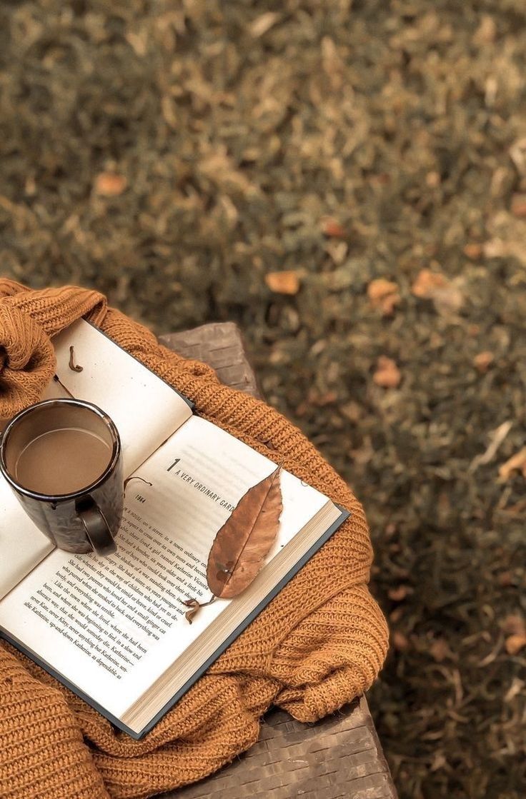 a cup of coffee and an open book on a bench