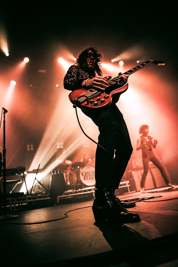 a man standing on top of a stage with a guitar in his hand and lights behind him