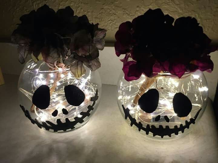 two glass vases with flowers in them sitting on a counter top, one decorated like jack - o - lanterns