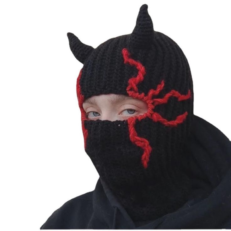 a young boy wearing a knitted devil mask with horns on it's face