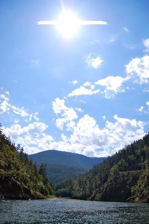 the sun shines brightly over a river with trees on both sides and mountains in the background