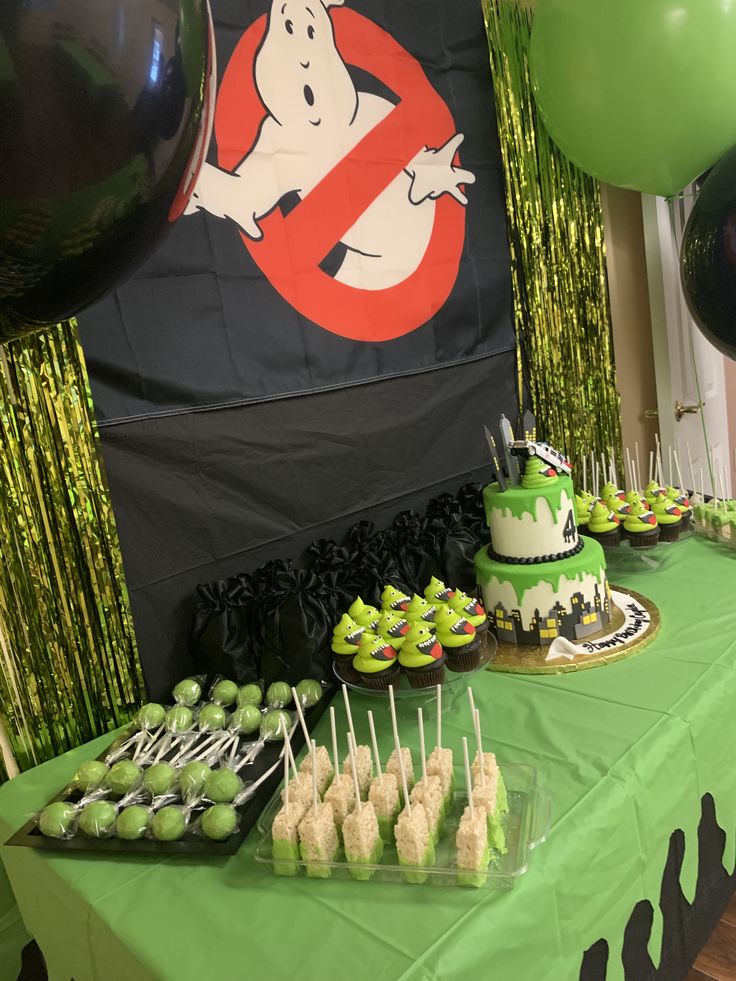 a table topped with cake and cupcakes covered in green frosting next to balloons