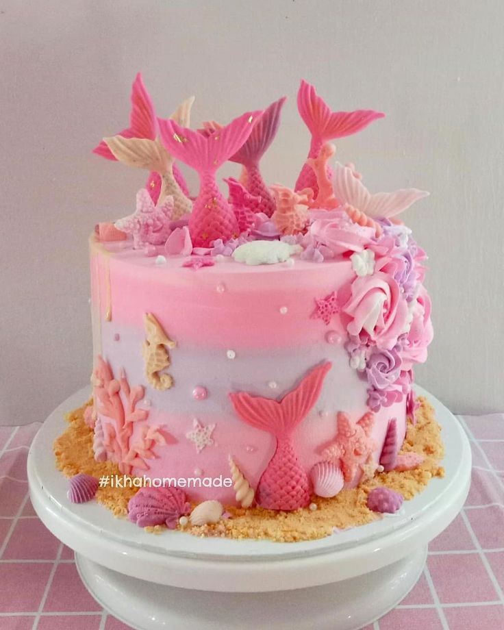 there is a pink and white cake with mermaid decorations on the top, sitting on a plate