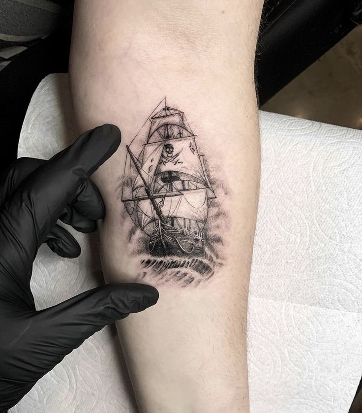 a person with a black and white tattoo on their arm holding up a small ship