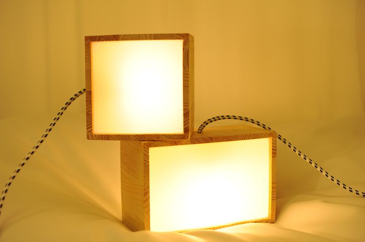 two square wooden lamps sitting next to each other on a white sheeted surface with black string