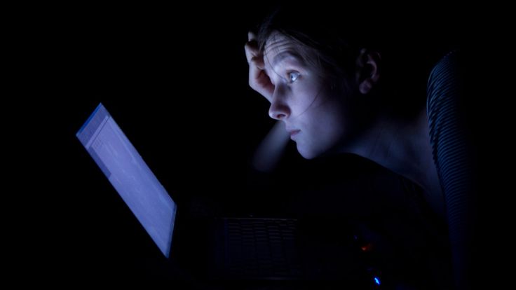 a young man sitting in the dark using a laptop computer at night with his eyes open