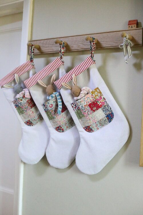 three white christmas stockings hanging from a wooden hanger with patchwork designs on them