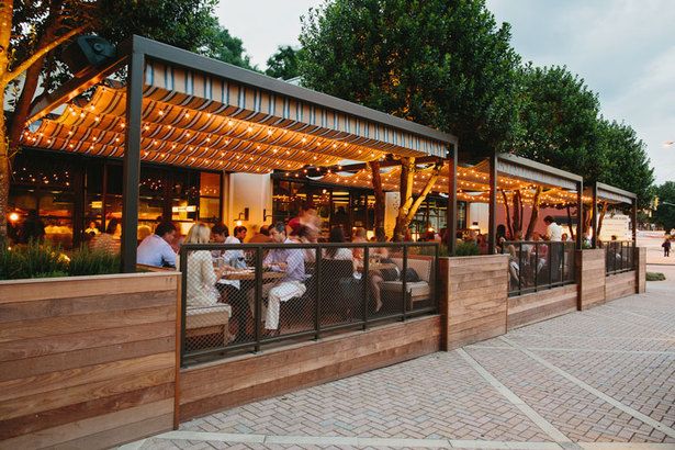 people sitting at tables in front of a restaurant with lights on the roof and outside