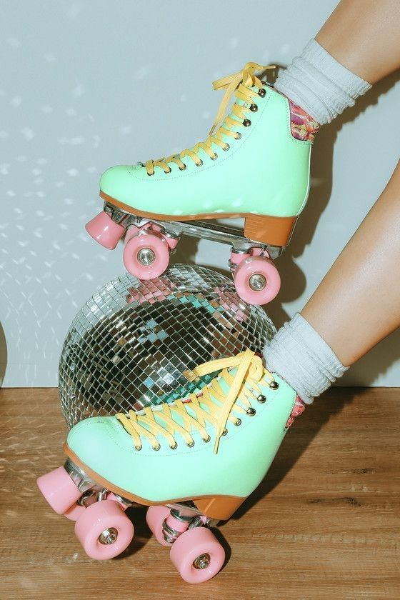 a pair of roller skates with pink and yellow wheels on a wooden floor next to a disco ball