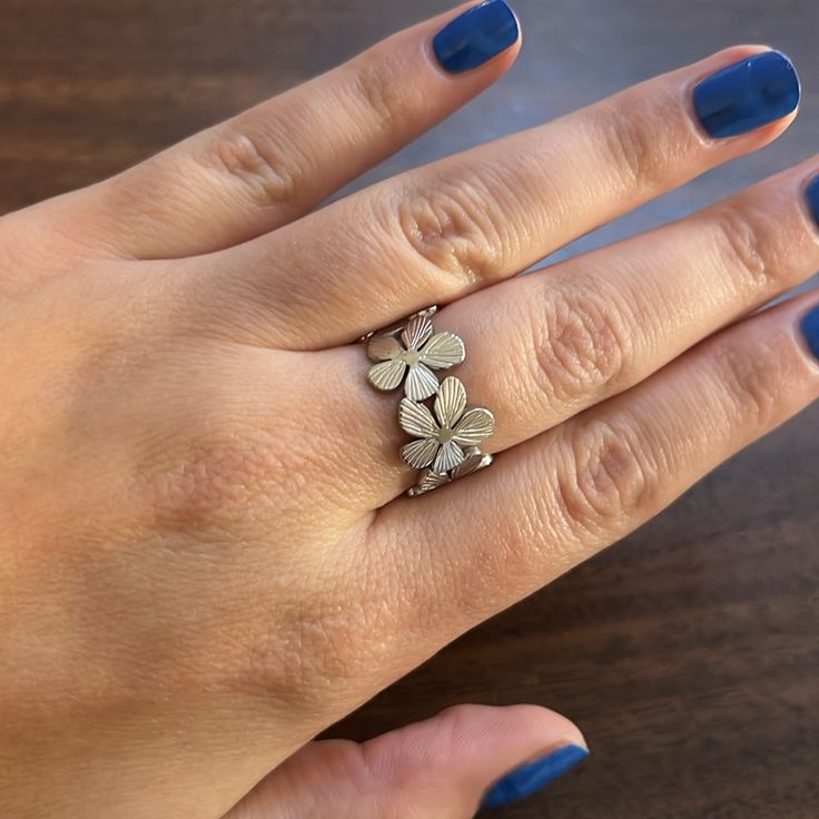 a woman's hand wearing a ring with four leaves on it and a blue manicure