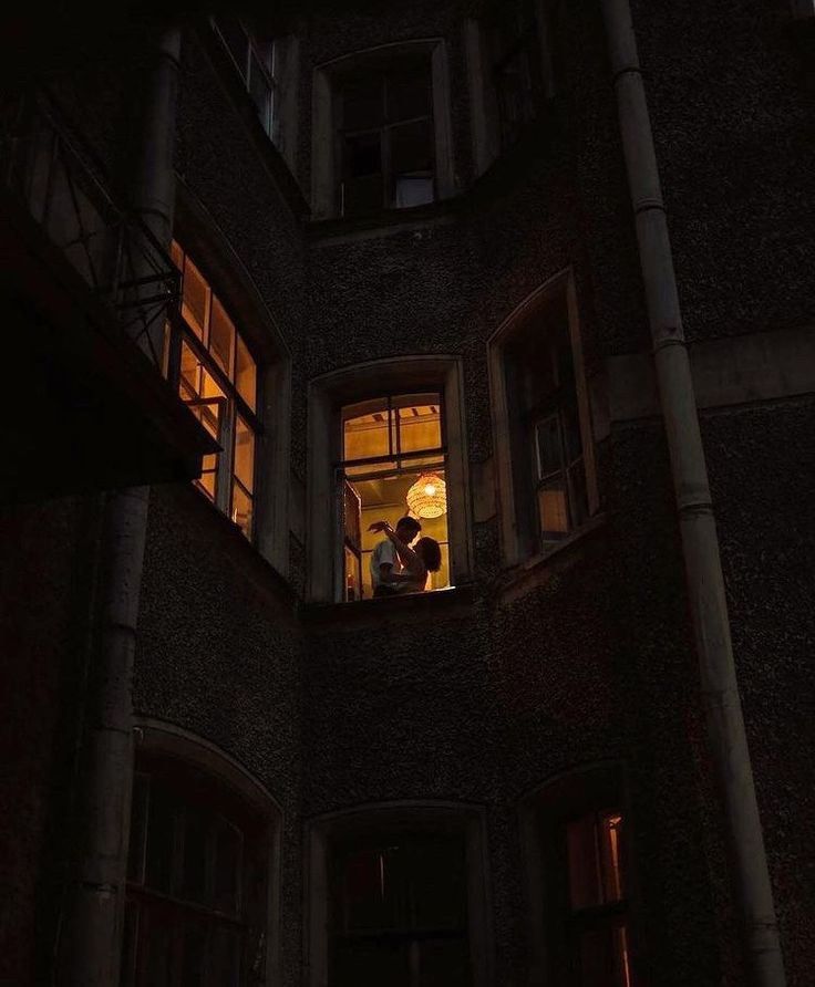 two people are standing in the window of an old building at night, looking out