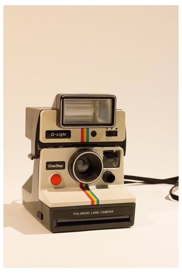 an old polaroid camera sitting on top of a white table next to a black cord