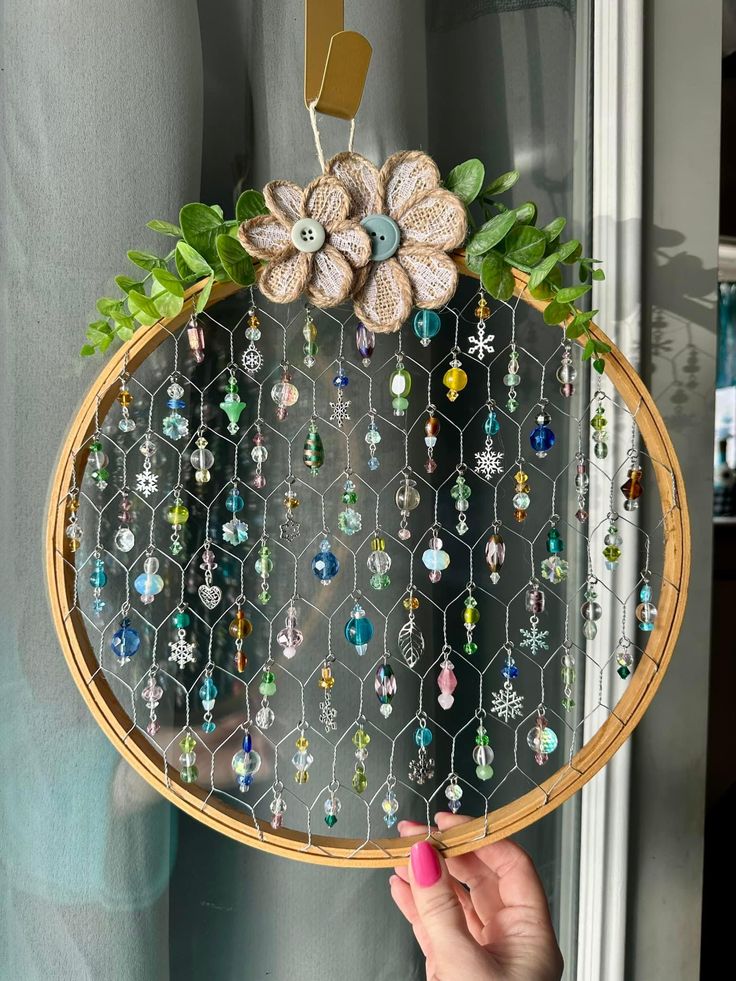 a person holding up a basket with flowers and beads on it in front of a window