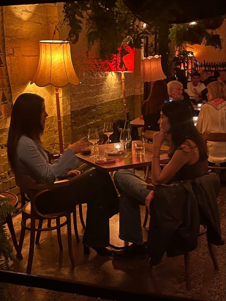 two women sitting at a table in a restaurant talking to each other and drinking wine