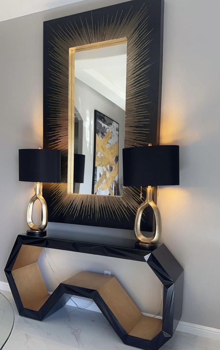 a black and gold console table with two lamps on it, in front of a mirror