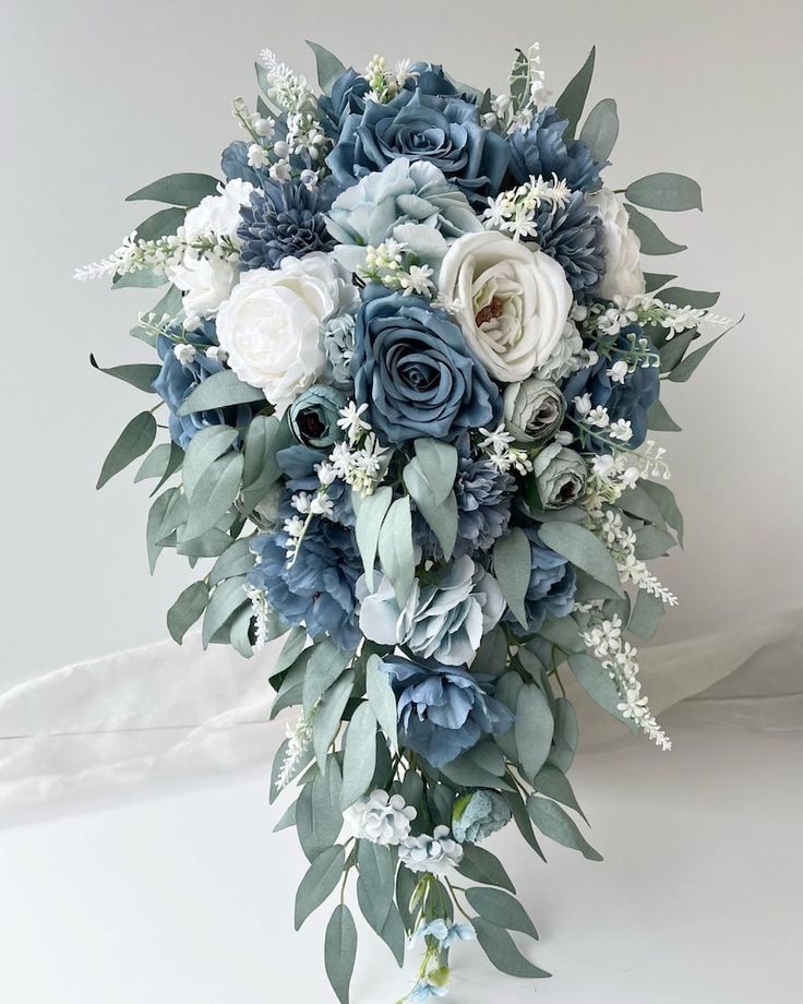 a bridal bouquet with blue flowers and greenery on the bottom, in front of a white background