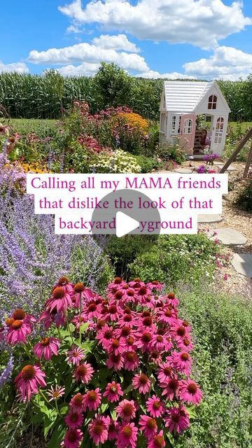 a garden filled with lots of flowers next to a white house and purple flowers in the foreground