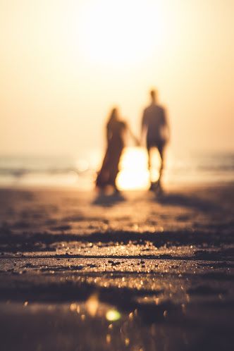 two people walking on the beach at sunset