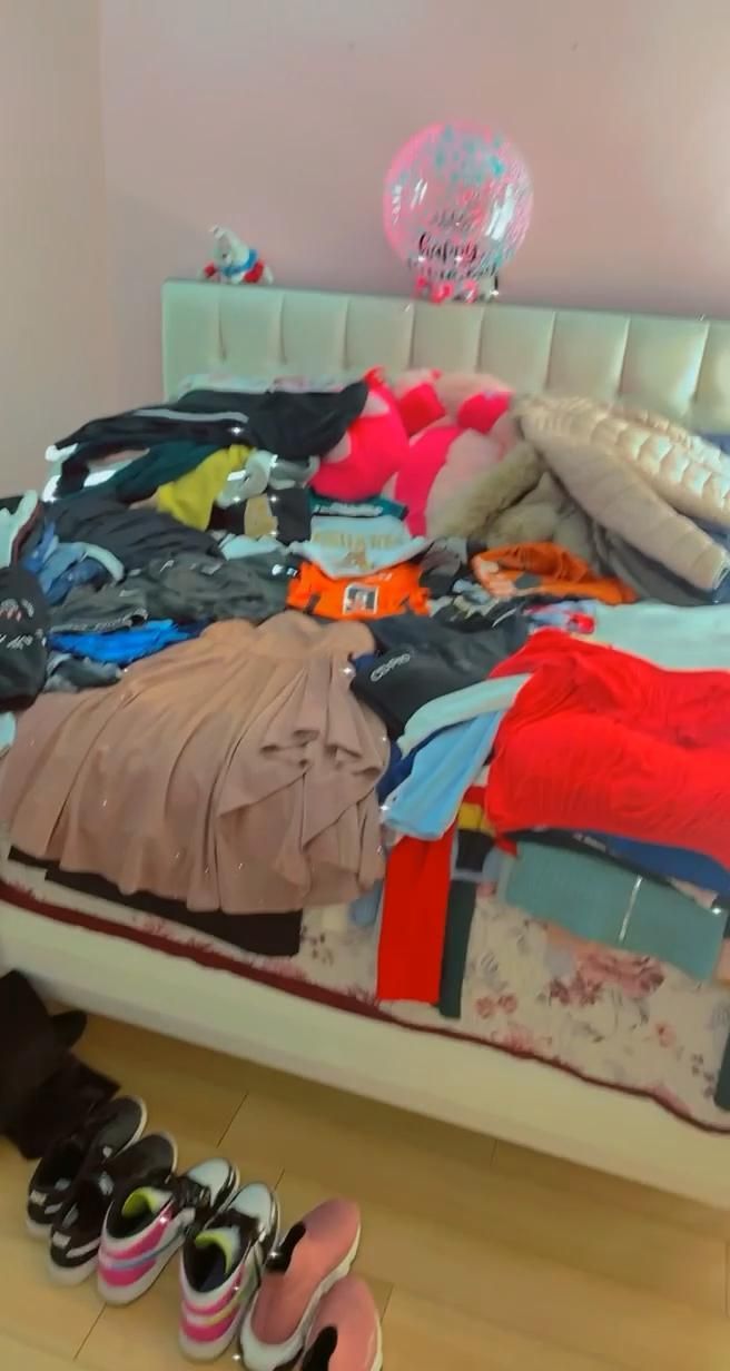 a bed with shoes on the floor next to it and a pile of clothes sitting on top of it