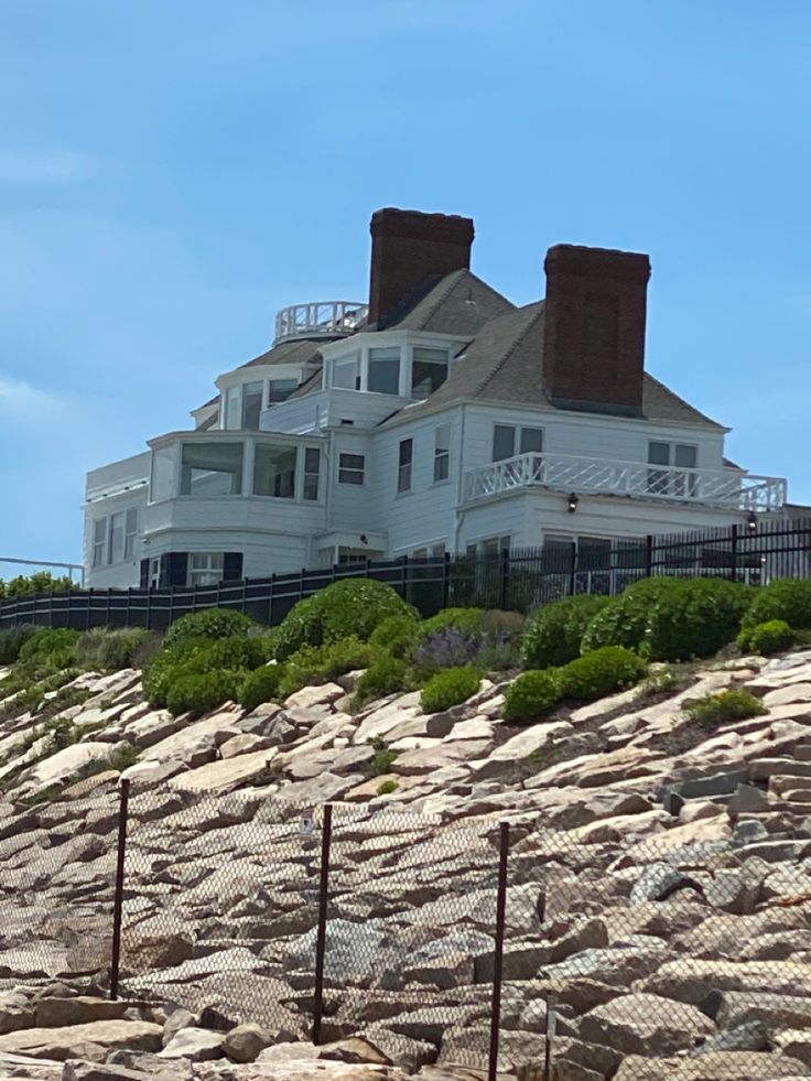 a large white house sitting on top of a rocky hill next to a fenced in area