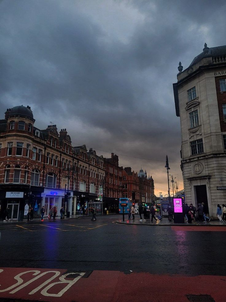 a city street with buildings and people walking on the side walk at night, under a cloudy sky