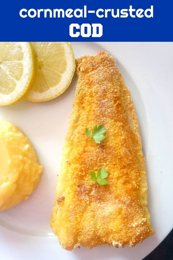 a white plate topped with fried fish next to lemon wedges