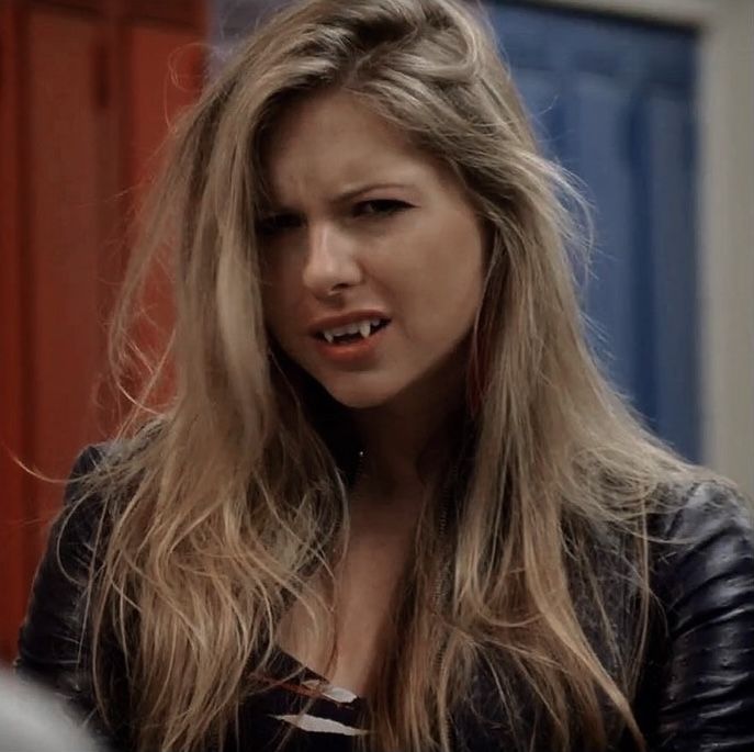 a woman with long blonde hair standing in front of a door and looking at the camera