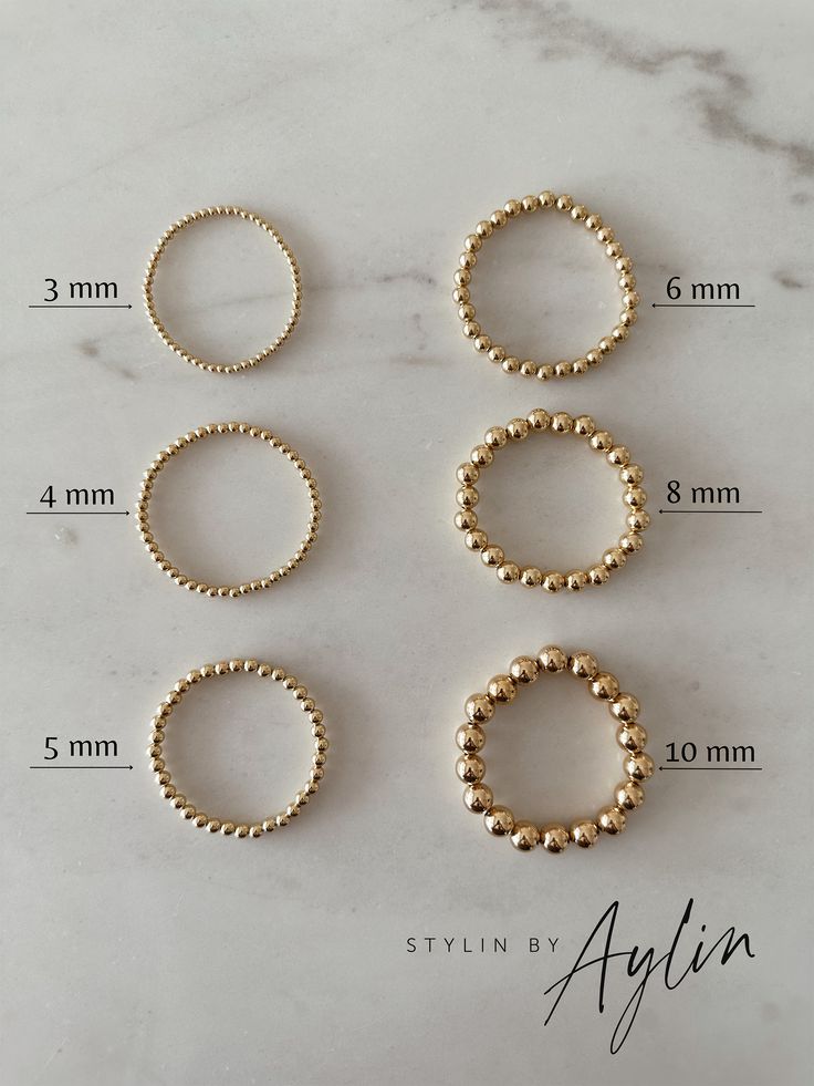 four gold beaded rings sitting on top of a white marble table with measurements for each ring