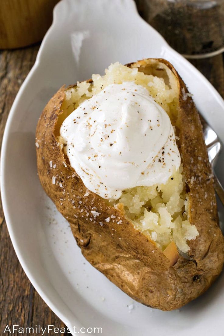 a baked potato with sour cream on top is sitting on a white plate next to a spoon