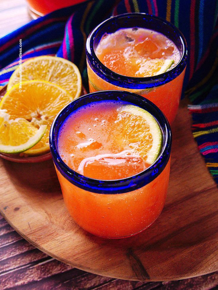 two glasses filled with orange juice on top of a wooden plate