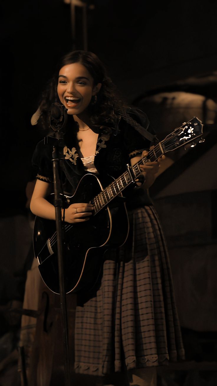 a woman holding a guitar and singing into a microphone