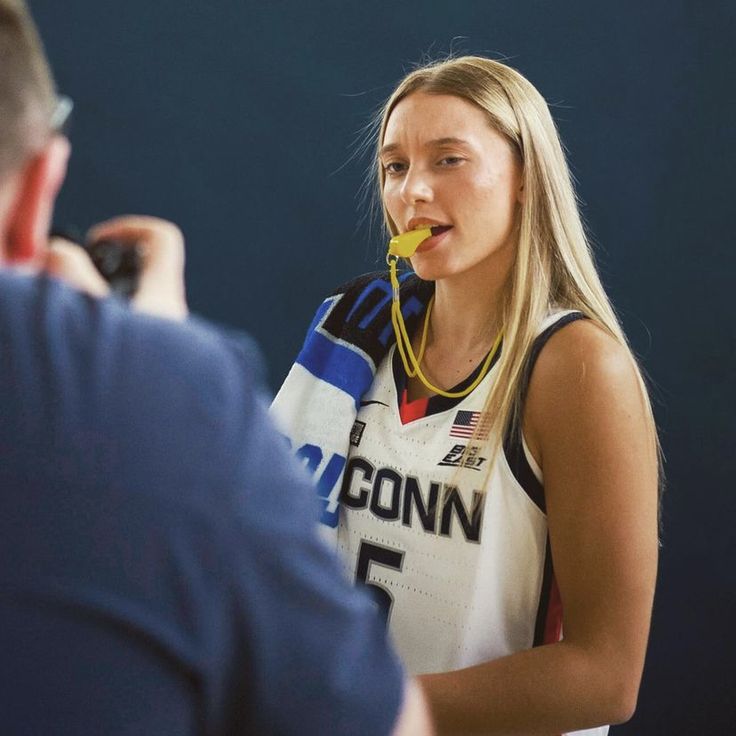 a female basketball player is being interviewed by an official in a sports uniform and holding a microphone to her ear