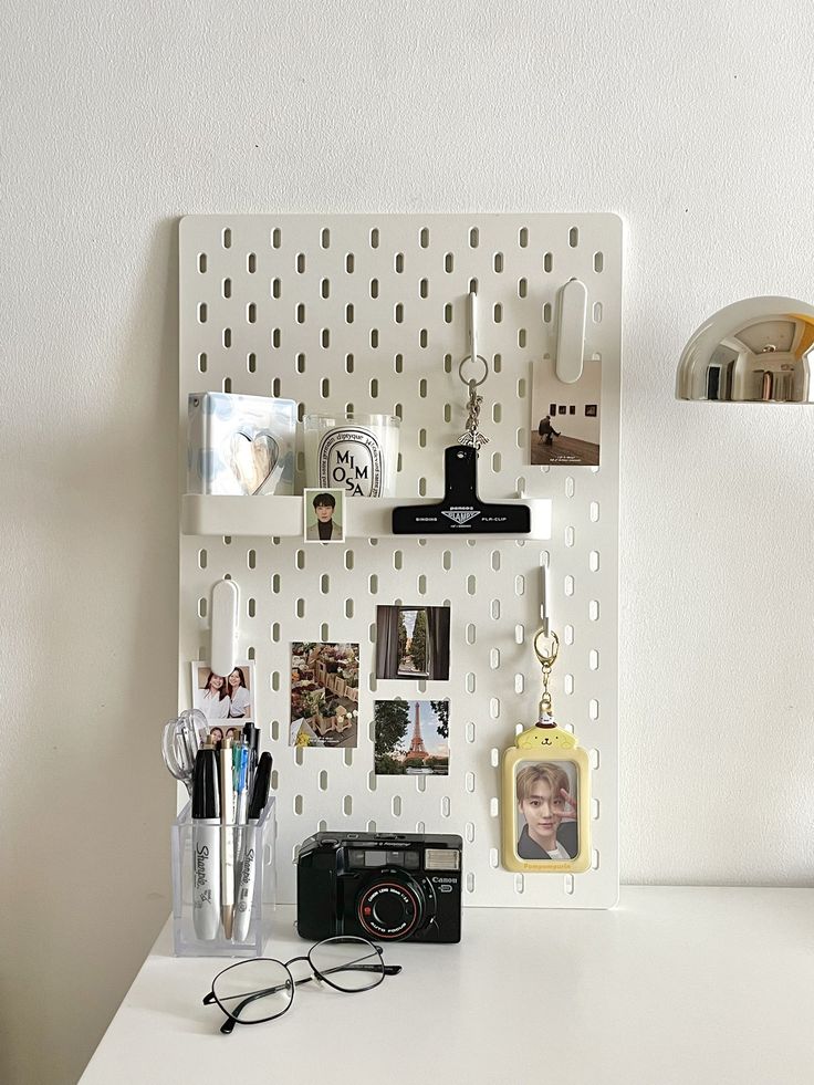 a white desk topped with a camera and other office supplies next to a wall mounted shelf