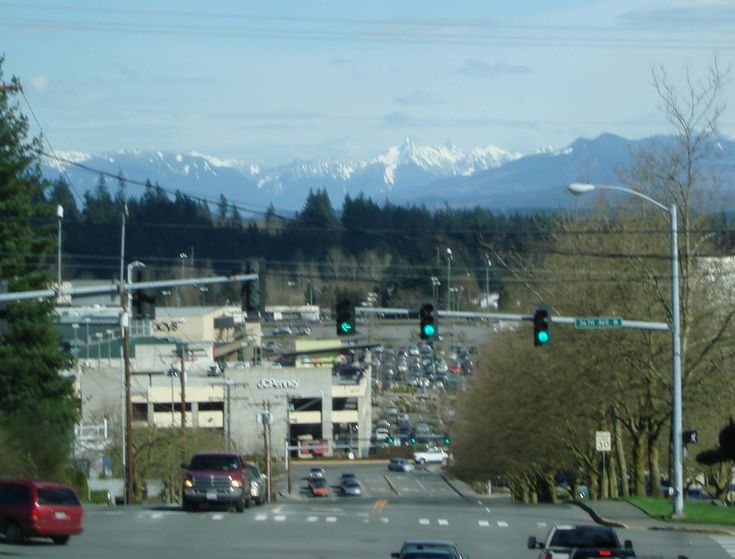 cars are driving down the street in front of snow capped mountain tops and green traffic lights