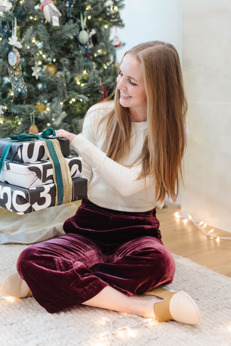 a woman sitting on the floor with her handbag in front of a christmas tree