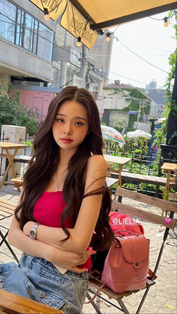 a young woman sitting on top of a wooden bench next to a pink bag and umbrella