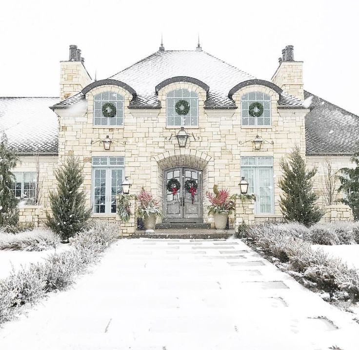 a large brick house with wreaths on it's front door and windows in the snow