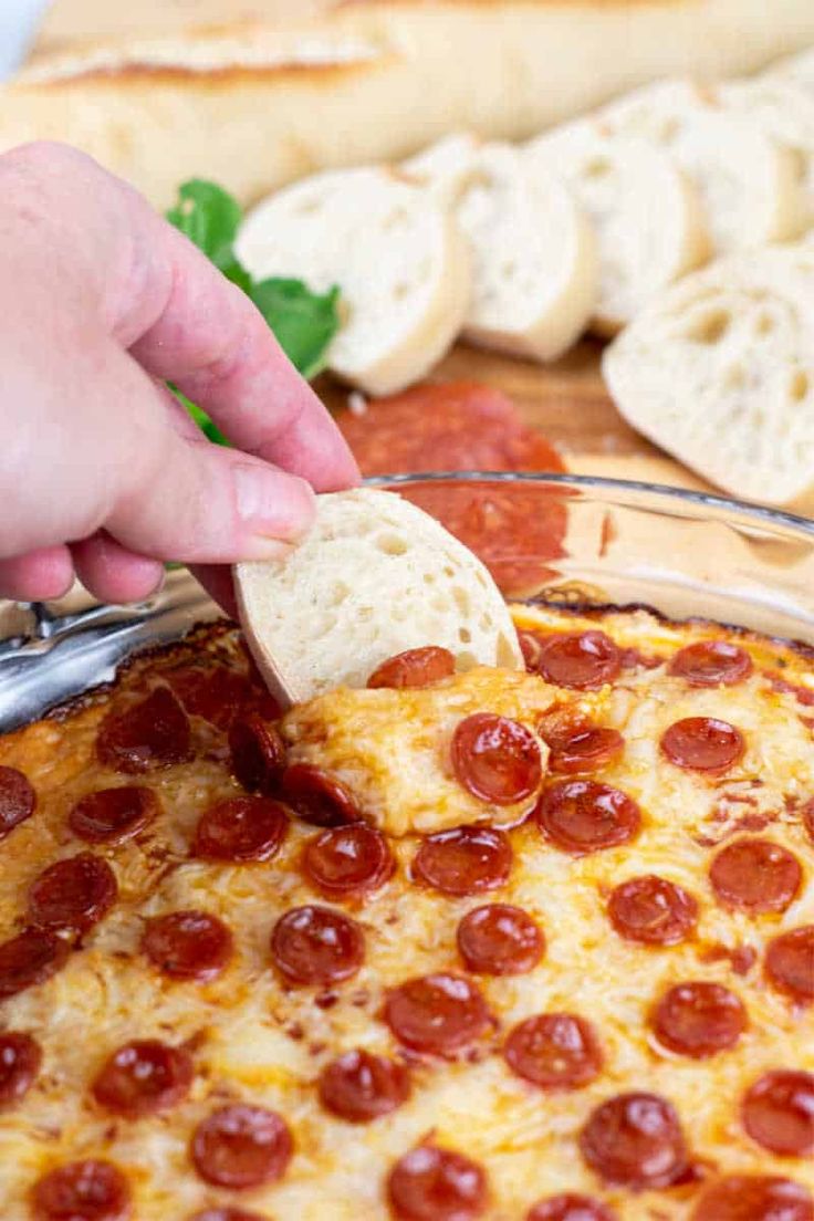 a person scooping cheese from a pizza in a glass dish with pepperoni on it