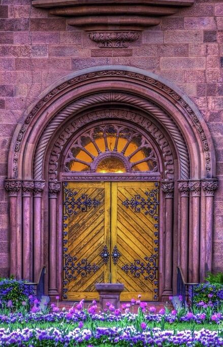 an old church door with purple flowers in the foreground