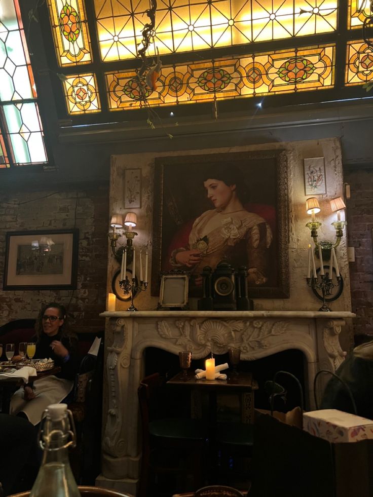 a man sitting at a table in front of a fire place with a painting on the wall