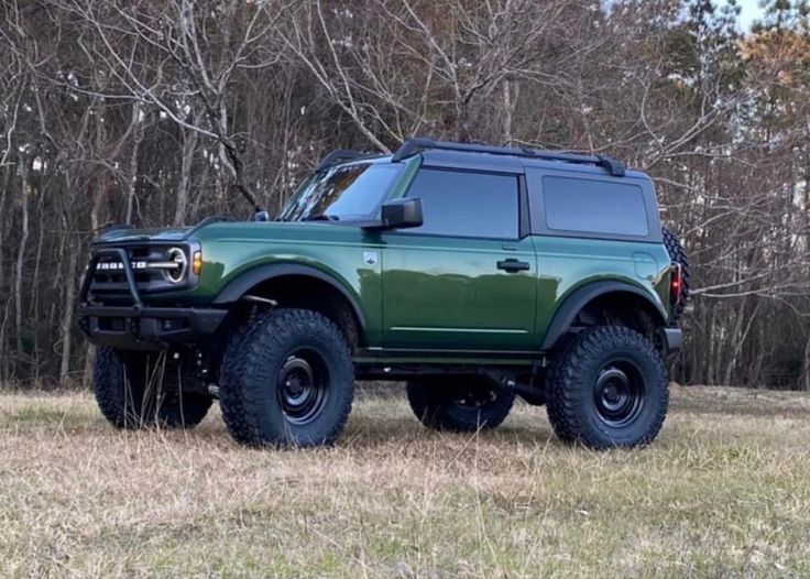 a large green truck parked on top of a grass covered field with trees in the background