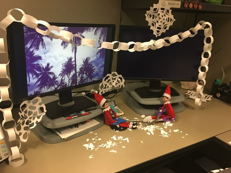 two elfs are sitting in front of a computer screen with paper chains on it