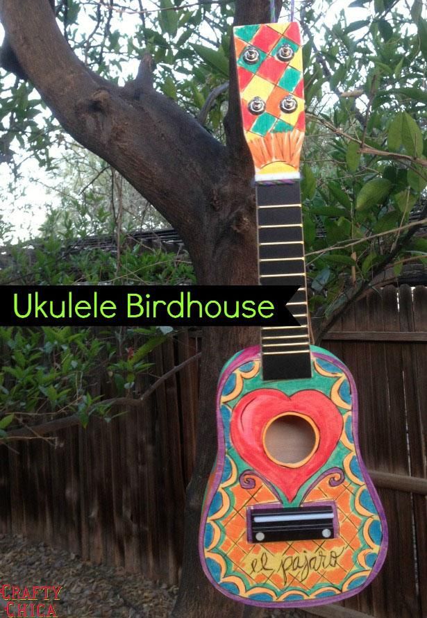 the ukulele birdhouse is hanging from a tree in front of a fence