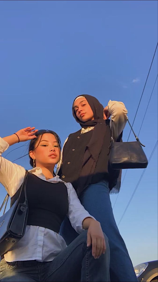 two women sitting on the back of a car while one woman holds her purse up to her ear