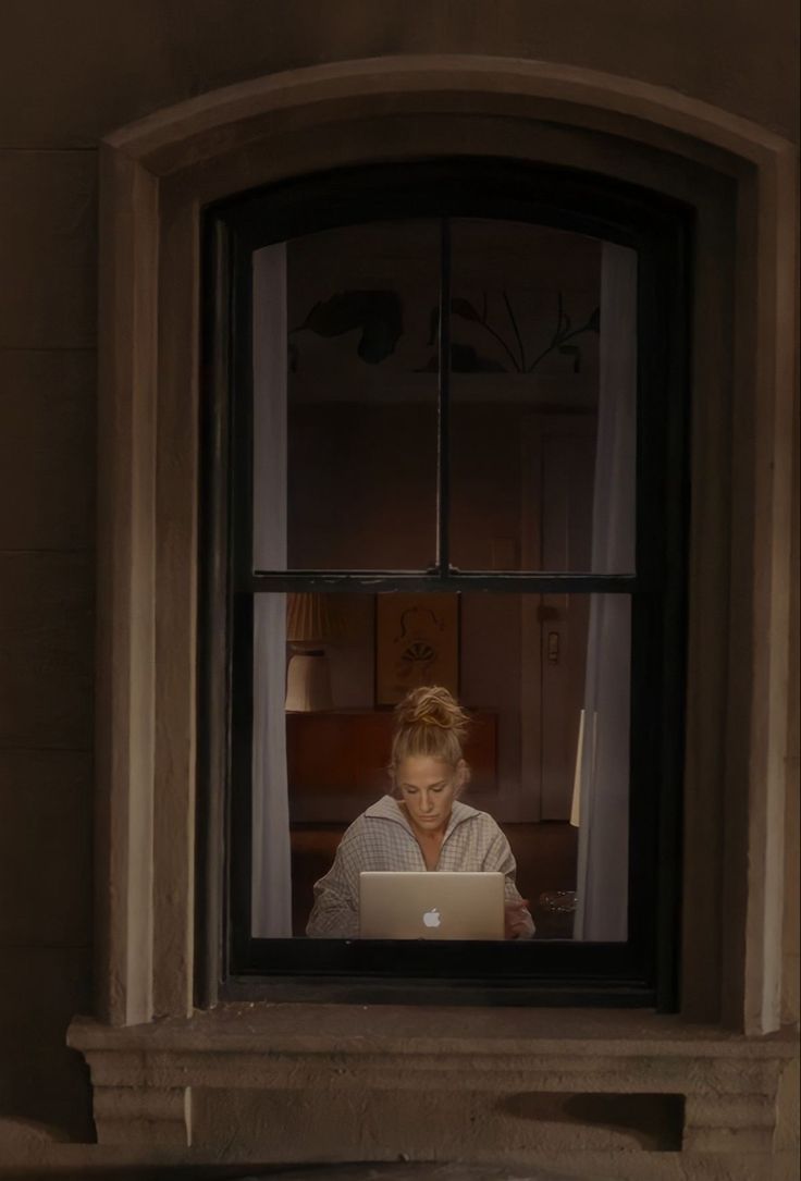 a woman sitting in front of a laptop computer on a window sill looking out