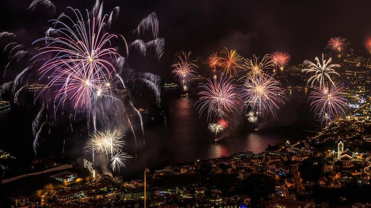 fireworks are lit up in the night sky over a city and water with buildings on both sides