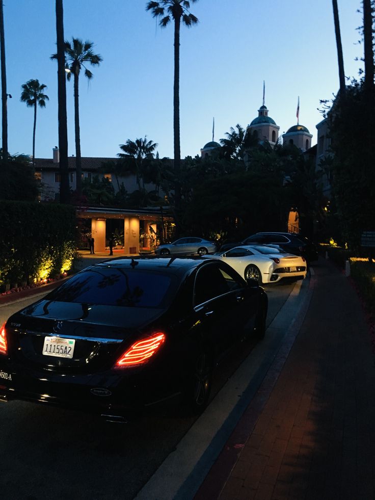 several cars parked on the side of a road at night with palm trees in the background